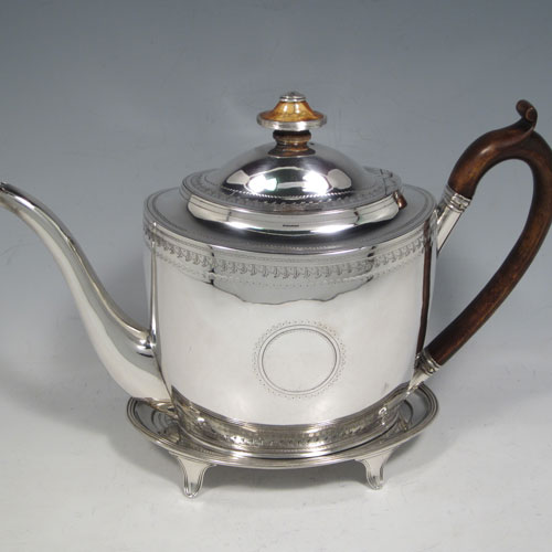 Antique Georgian sterling silver teapot on stand, having a hand-engraved oval body, with bands of floral decoration, a hinged domed lid with silver bound ivory finial, a wooden scroll handle, and sitting on its original stand with four flanged feet and reeded border. Made by Thomas Robins of London in 1800. The dimensions of this fine hand-made silver teapot on stand are length 28 cms (11 inches), height (on stand) 19 cms (7.5 inches), and it weighs approx. 543g (17.5 troy ounces).