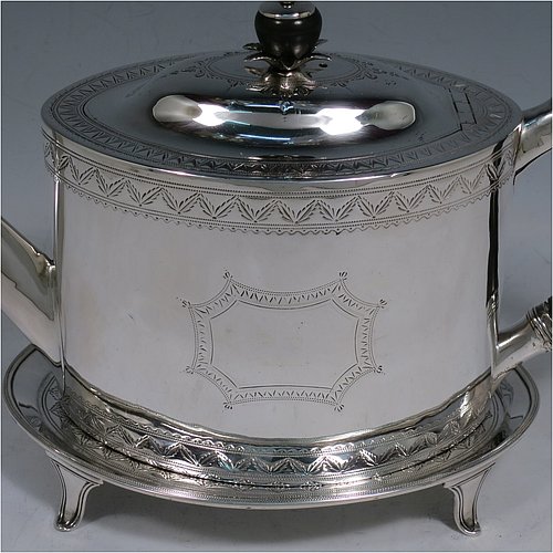 An Antique Georgian Sterling Silver teapot on stand, having a hand-engraved oval body, with bands of floral decoration, a hinged domed lid with silver bound wooden finial and flat hidden hinge, a wooden scroll handle, and sitting on its original stand with four flanged feet and reeded border. Made by Joseph Scammell of London in 1790. The dimensions of this fine hand-made antique silver teapot on stand are length 28 cms (11 inches), height (on stand) 16 cms (6.25 inches), and it weighs approx. 527g (17 troy ounces).   