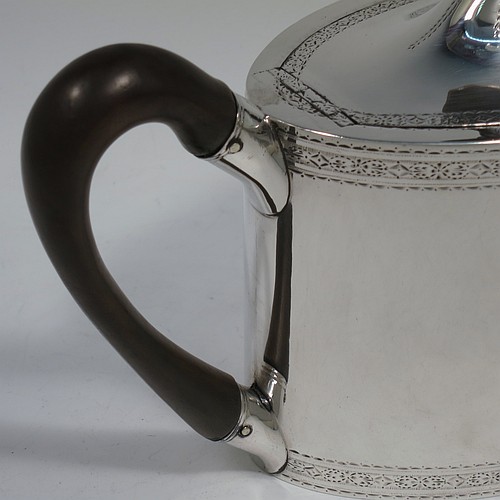 A very handsome Neoclassical style Antique Georgian Sterling Silver teapot, having an oval straight-sided body with hand-engraved upper and lower bands of floral work, with oval engraved cartouches on both sides, a straight tapering spout, a wooden scroll handle and oval finial, an invisibly hinged domed lid with matching engraving, and all sitting on a flat base. Made by William Turton of London in 1785, with a rare Incuse Duty Mark. The dimensions of this fine hand-made antique silver teapot are length 27 cms (10.5 inches), height 15 cms (6 inches), and it weighs approx. 350g (11.3 troy ounces). Please note that this item is crested.