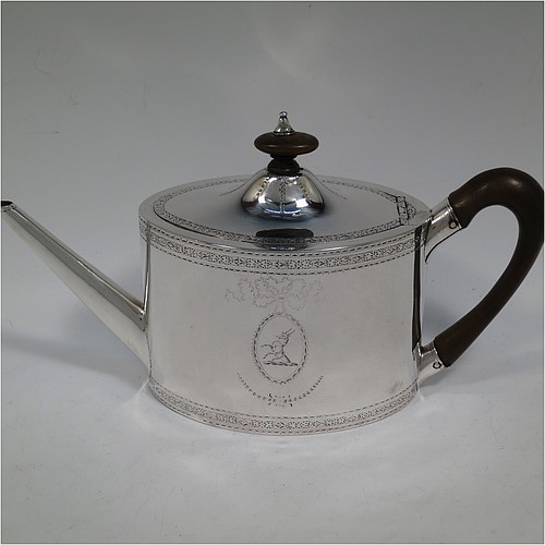 A very handsome Neoclassical style Antique Georgian Sterling Silver teapot, having an oval straight-sided body with hand-engraved upper and lower bands of floral work, with oval engraved cartouches on both sides, a straight tapering spout, a wooden scroll handle and oval finial, an invisibly hinged domed lid with matching engraving, and all sitting on a flat base. Made by William Turton of London in 1785, with a rare Incuse Duty Mark. The dimensions of this fine hand-made antique silver teapot are length 27 cms (10.5 inches), height 15 cms (6 inches), and it weighs approx. 350g (11.3 troy ounces). Please note that this item is crested.