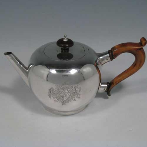 Antique Georgian sterling silver teapot in an early George II Bullet style, having a plain round baluster body, straight tapering spout, wooden scroll handle and finial, an invisibly hinged flat lid, and sitting on a collet foot. Made by George Greenhill Jones of London in 1730. The dimensions of this fine hand-made silver teapot are length 21 cms (8.25 inches), height 11 cms (4.3 inches), and it weighs approx. 445g (14.4 troy ounces). Please note that this teapot is crested on one side with a full armorial crest.  