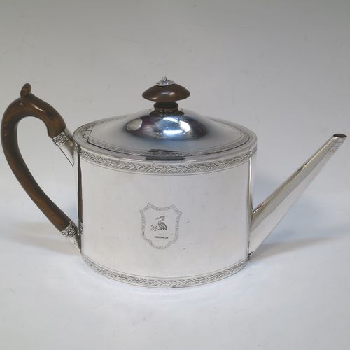 A very handsome Neoclassical style Antique Georgian Sterling Silver teapot, having an oval straight-sided body with hand-engraved upper and lower bands of floral work, with engraved cartouches on both sides, a straight tapering spout, a wooden scroll handle and oval finial, an invisibly hinged domed lid with matching engraving, and all sitting on a flat base. Made by Henry Chawner of London in 1794. The dimensions of this fine hand-made antique silver teapot are length 26 cms (10 inches), height 15 cms (6 inches), and it weighs approx. 350g (11.3 troy ounces). Please note that this item is crested.  