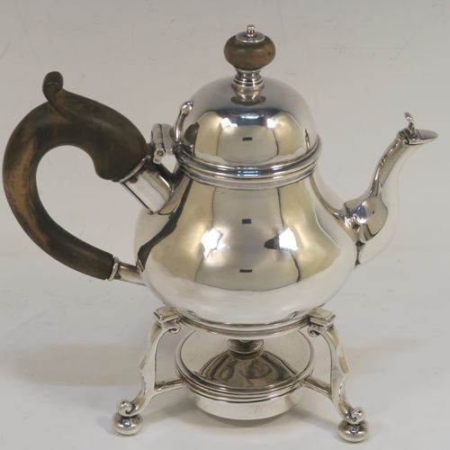 A very rare and unusual Sterling Silver bachelor sized teapot and burner stand, in a George I style with a plain round bellied body, having a hinged domed lid with wooden finial, a wooden insulated handle, a curved spout with a hinged lid, and all sitting on an original burner stand with three scroll feet and a plain round removable wick burner. This elegant silver teapot and burner stand was made by Rodney C. Pettit of London in 1981. The dimensions of this fine hand-made silver teapot and stand are height 17 cms (6.75 inches), length 17.5 cms (7 inches), and it weighs approx. 500g (16 troy ounces).  