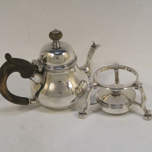 A very rare and unusual Sterling Silver bachelor sized teapot and burner stand, in a George I style with a plain round bellied body, having a hinged domed lid with wooden finial, a wooden insulated handle, a curved spout with a hinged lid, and all sitting on an original burner stand with three scroll feet and a plain round removable wick burner. This elegant silver teapot and burner stand was made by Rodney C. Pettit of London in 1981. The dimensions of this fine hand-made silver teapot and stand are height 17 cms (6.75 inches), length 17.5 cms (7 inches), and it weighs approx. 500g (16 troy ounces).  