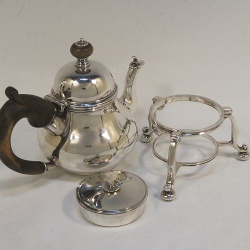 A very rare and unusual Sterling Silver bachelor sized teapot and burner stand, in a George I style with a plain round bellied body, having a hinged domed lid with wooden finial, a wooden insulated handle, a curved spout with a hinged lid, and all sitting on an original burner stand with three scroll feet and a plain round removable wick burner. This elegant silver teapot and burner stand was made by Rodney C. Pettit of London in 1981. The dimensions of this fine hand-made silver teapot and stand are height 17 cms (6.75 inches), length 17.5 cms (7 inches), and it weighs approx. 500g (16 troy ounces).  