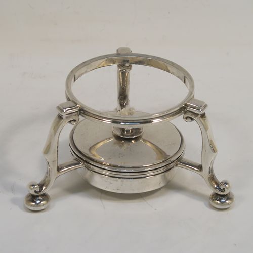 A very rare and unusual Sterling Silver bachelor sized teapot and burner stand, in a George I style with a plain round bellied body, having a hinged domed lid with wooden finial, a wooden insulated handle, a curved spout with a hinged lid, and all sitting on an original burner stand with three scroll feet and a plain round removable wick burner. This elegant silver teapot and burner stand was made by Rodney C. Pettit of London in 1981. The dimensions of this fine hand-made silver teapot and stand are height 17 cms (6.75 inches), length 17.5 cms (7 inches), and it weighs approx. 500g (16 troy ounces).  