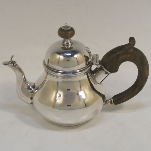 A very rare and unusual Sterling Silver bachelor sized teapot and burner stand, in a George I style with a plain round bellied body, having a hinged domed lid with wooden finial, a wooden insulated handle, a curved spout with a hinged lid, and all sitting on an original burner stand with three scroll feet and a plain round removable wick burner. This elegant silver teapot and burner stand was made by Rodney C. Pettit of London in 1981. The dimensions of this fine hand-made silver teapot and stand are height 17 cms (6.75 inches), length 17.5 cms (7 inches), and it weighs approx. 500g (16 troy ounces).  