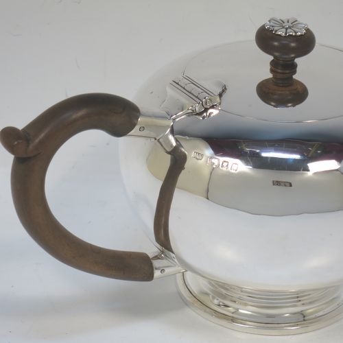 A very handsome Sterling Silver bachelor size teapot in an early George II Bullet or Skittle Ball style, having a plain round bellied body, a curved spout, a wooden scroll handle and finial with silver mount, a hinged lid, and sitting on a pedestal foot. Made by Mappin and Webb of London in 1926. The dimensions of this fine hand-made silver bachelor teapot are length 23 cms (9 inches), height 12 cms (4.75 inches), and it weighs approx. 350g (11.3 troy ounces).   