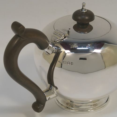 A very handsome Sterling Silver teapot in an early George II Bullet or Skittle Ball style, having a very plain round bellied body, a straight tapering spout, a wooden scroll handle and finial, a hinged flat lid, and sitting on a pedestal foot. This elegant silver teapot was made by Wakely and Wheeler of London in 1936. The dimensions of this fine hand-made silver skittle ball style teapot are length 20 cms (8 inches), height 12 cms (4.75 inches), and it weighs approx. 280g (9 troy ounces).   