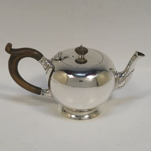 A very handsome Sterling Silver bachelor sized teapot in an early George II Bullet or Skittle Ball style, having a very plain round bellied body, a wooden scroll handle and finial, a hinged lid, and sitting on a pedestal foot. This elegant silver teapot was made by Carrington and Co., of London in 1907. The dimensions of this fine hand-made silver skittle ball style teapot are length 19 cms (7.5 inches), height 10 cms (4 inches), and it weighs approx. 250g (8 troy ounces).   