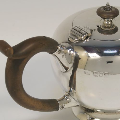 A very handsome Sterling Silver bachelor sized teapot in an early George II Bullet or Skittle Ball style, having a very plain round bellied body, a wooden scroll handle and finial, a hinged lid, and sitting on a pedestal foot. This elegant silver teapot was made by Carrington and Co., of London in 1907. The dimensions of this fine hand-made silver skittle ball style teapot are length 19 cms (7.5 inches), height 10 cms (4 inches), and it weighs approx. 250g (8 troy ounces).   