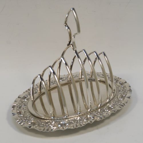 A very pretty Antique Victorian Silver Plated seven-bar toast-rack, having seven arch-shaped and graduated wire-work toast holders, attached to a crumb plate with a hand-chased scroll and floral decorated border, and all sitting on four ball feet. This beautiful antique toastrack was made by Joseph Rogers of Sheffield in ca. 1880. The dimensions of this fine hand-made antique silver-plated toast-rack are length 18 cms (7 inches), height 15 cms (6 inches), and width 13 cms (5 inches).   