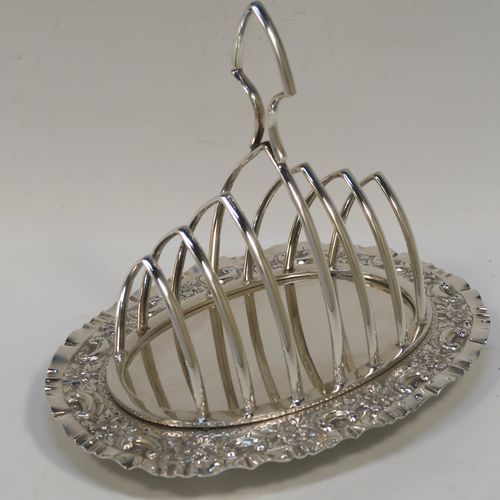 A very pretty Antique Victorian Silver Plated seven-bar toast-rack, having seven arch-shaped and graduated wire-work toast holders, attached to a crumb plate with a hand-chased scroll and floral decorated border, and all sitting on four ball feet. This beautiful antique toastrack was made by Joseph Rogers of Sheffield in ca. 1880. The dimensions of this fine hand-made antique silver-plated toast-rack are length 18 cms (7 inches), height 15 cms (6 inches), and width 13 cms (5 inches).   