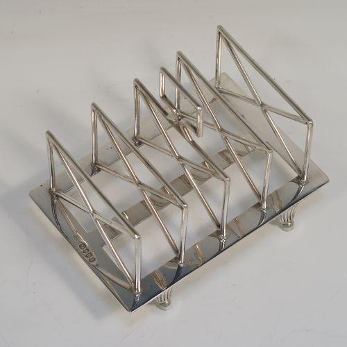 A very unusual Arts and Crafts style Antique Victorian Sterling Silver five-bar toastrack, having  square crossed wire-work bars, with a square loop handle, and sitting on a base with a strengthening strut and four fluted and flanged feet. This elegant Arts and Crafts silver toast-rack was made by Edward Hutton of London in 1881. The dimensions of this fine hand-made antique silver toast-rack are length 12.5 cms (5 inches), height 11 cms (4.3 inches), width 9 cms (3.5 inches), and it weighs approx. 259g (8.4 troy ounces).   