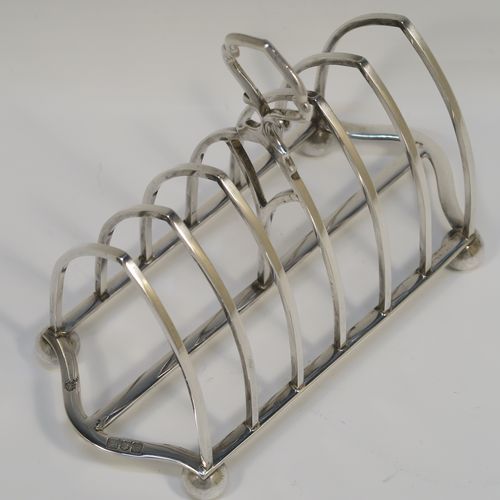 A large and very handsome Antique Edwardian Sterling Silver seven-bar toastrack, having plain arched cross-section wire-work bars, a matching  loop handle, all sitting on a rectangular base with a strengthening strut, on four ball feet. This elegant antique silver toast-rack was made by William Hutton and Sons of London in 1902. The dimensions of this fine hand-made antique silver toast-rack are length 18 cms (7 inches), height 15 cms (6 inches), width 9 cms (3.5 inches), and it weighs approx. 297g (9.6 troy ounces).  