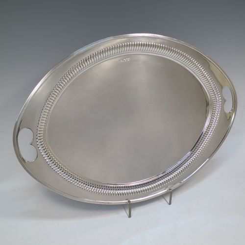 A very pretty Antique Victorian Sterling Silver oval two-handled tea tray, having a plain ground, with straight-fluted border and applied reeded edge, all sitting on a flat base. This very handsome silver tray was made by James Walter Deakin of Sheffield in 1892. The dimensions of this fine hand-made silver tray are length 46 cms (18 inches), width 32 cms (12.5 inches), and it weighs approx. 1,125g (36.3 troy ounces).  