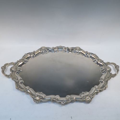 A very elegant Antique Edwardian Sterling Silver tray, having a shaped oval body with a plain ground, an applied shell and scroll border, and two cast side-handles, all sitting on a flat base. This classical silver tray was made by George Howson of Sheffield in 1902. The dimensions of this fine hand-made antique silver tray are length (inc. handles) 74 cms (29 inches), width 48 cms (19 inches), and it weighs approx. 3,510g (117 troy ounces).  