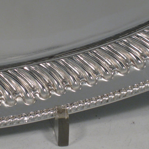 Antique Victorian sterling silver oval two-handled tea tray, having a plain ground, with swirl-fluted border and applied gadroon edge, all sitting on a flat base. This very handsome silver tray was made by Henry Holland of Sheffield in 1888. The dimensions of this fine hand-made silver tray are length 46 cms (18 inches), width 26.5 cms (10.5 inches), and it weighs approx. 891g (28.7 troy ounces).