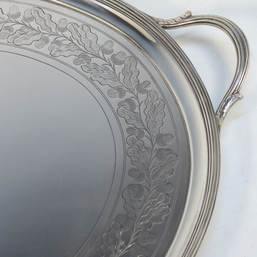 A very elegant Antique Georgian Sterling Silver tray, having an oval body with a plain central ground surrounded by a band of hand-engraved acorn and oak leaf decoration, with an applied reeded border, and two cast reeded handles, all sitting on four cast flange feet. This beautiful antique silver tray was made by Peter, Anne, and William Bateman of London in 1802. The dimensions of this fine hand-made antique silver tray are length (inc. handles) 55 cms (21.75 inches), width 35.5 cms (14 inches), height 4.5 cms (1.75 inches), and it weighs approx. 1,795g (58 troy ounces).   