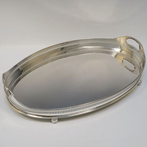 A very handsome Antique Victorian Sterling Silver galleried drinks tray, having an oval body with a hand-pierced gallery, with two oval cut-out side-handles, an applied bead-edged top border, a plain oval ground, and sitting on four cast ball feet. This elegant antique silver drinks tray was made by John Newton Mappin of London in 1896. The dimensions of this fine hand-made silver gallery tray are length 39 cms (15.3 inches), width 26.5 cms (10.5 inches), and it weighs approx. 1,115g (36 troy ounces).   