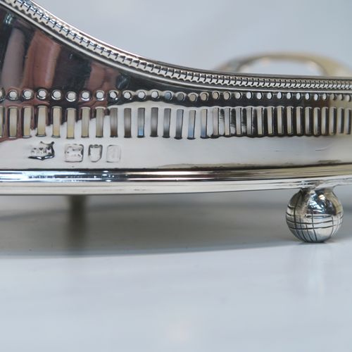 A very handsome Antique Victorian Sterling Silver galleried drinks tray, having an oval body with a hand-pierced gallery, with two oval cut-out side-handles, an applied bead-edged top border, a plain oval ground, and sitting on four cast ball feet. This elegant antique silver drinks tray was made by John Newton Mappin of London in 1896. The dimensions of this fine hand-made silver gallery tray are length 39 cms (15.3 inches), width 26.5 cms (10.5 inches), and it weighs approx. 1,115g (36 troy ounces).   