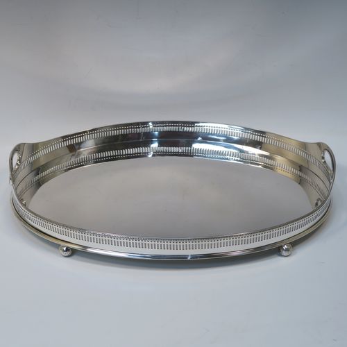 A very handsome Antique Victorian Sterling Silver galleried drinks tray, having an oval body with a hand-pierced gallery, with two oval cut-out side-handles, an applied bead-edged top border, a plain oval ground, and sitting on four cast ball feet. This elegant antique silver drinks tray was made by John Newton Mappin of London in 1896. The dimensions of this fine hand-made silver gallery tray are length 39 cms (15.3 inches), width 26.5 cms (10.5 inches), and it weighs approx. 1,115g (36 troy ounces).   