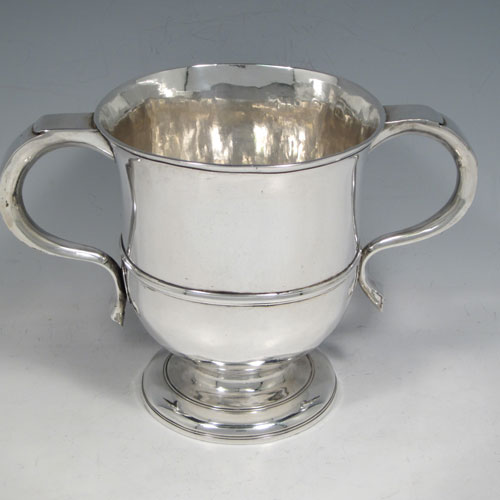 Antique Georgian George II Sterling silver trophy loving cup, having a plain round body with central reeded band, two scroll side-handles which are part-marked with a makers mark, and sitting on a pedestal foot. Made by Benjamin Blakely of London in 1738. The dimensions of this fine silver loving cup are height 14.5 cms (5.75 inches), spread across handles 23 cms (9 inches), and it weighs approx. 511g (16.5 troy ounces).