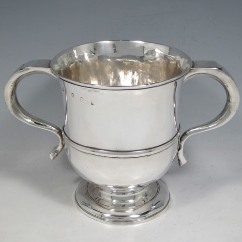 Antique Georgian George II Sterling silver trophy loving cup, having a plain round body with central reeded band, two scroll side-handles which are part-marked with a makers mark, and sitting on a pedestal foot. Made by Benjamin Blakely of London in 1738. The dimensions of this fine silver loving cup are height 14.5 cms (5.75 inches), spread across handles 23 cms (9 inches), and it weighs approx. 511g (16.5 troy ounces).