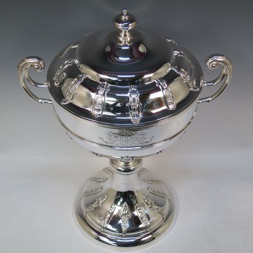 A very impressive and large Antique Edwardian  Sterling Silver trophy cup and cover, having a round body with applied floral strap-work decoration, two flying scroll side-handles, a central applied girdle band, a pull-off lid with matching applied strap-work and a cast round finial, and all sitting on a stepped pedestal foot, again, with matching decoration. Made by Alexander Clark of Sheffield in 1906. The dimensions of this fine hand-made antique silver trophy cup and cover are height 48 cms (19 inches), spread across arms 37 cms (14.5 inches), and it weighs approx. 2,842g (92 troy ounces). Please note that this item has a full armorial crest engraved on one side. 