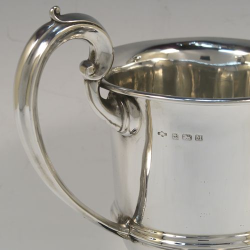 An elegant Sterling Silver trophy loving cup and plinth, having a plain round body with a central reeded band, two scroll side-handles, and sitting on a round pedestal foot, and original black Bakelite plinth. This handsome silver loving cup trophy was made by A. E. Poston & Co., of Birmingham in 1936. The dimensions of this fine silver loving trophy cup are (without plinth) height 16.5 cms (6.5 inches), spread across handles 20 cms (8 inches), and it weighs approx. 240g (7.7 troy ounces).  