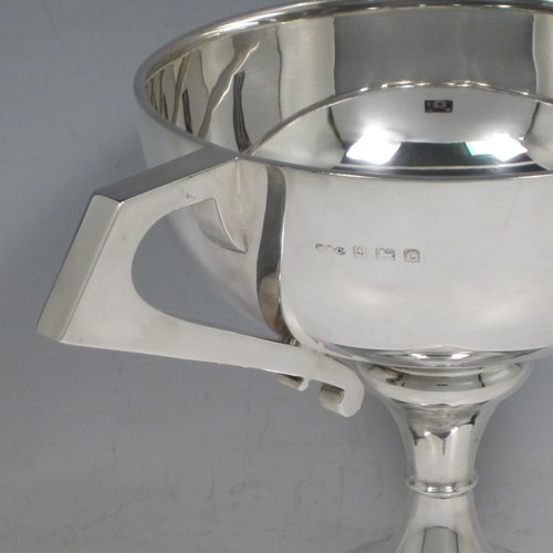 Sterling silver trophy cup, in an Art Deco style having two angular handles, a plain round body, and sitting on a pedestal foot with a square base. Made by the Wilmot Manufacturing Co., of Birmingham in 1927. The dimensions of this fine silver trophy cup are height 15 cms (6 inches), spread across handles 23.5 cms (9.25 inches), and it weighs approx. 361g (11 troy ounces).   