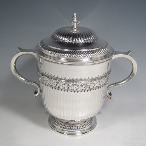 Antique Sterling silver trophy cup and cover, in a George II style, having a round body with hand-chased fluted and floral decoration, two scroll side-handles, a pull-off lid with cast finial, and sitting on a pedestal foot. Made Johnson, Walker & Tolehurst of London in 1912. The dimensions of this fine hand-made silver trophy cup and cover are height 24 cms (9.5 inches), spread across arms 26.5 cms (10.5 inches), and it weighs approx. 1,056g (34 troy ounces).   