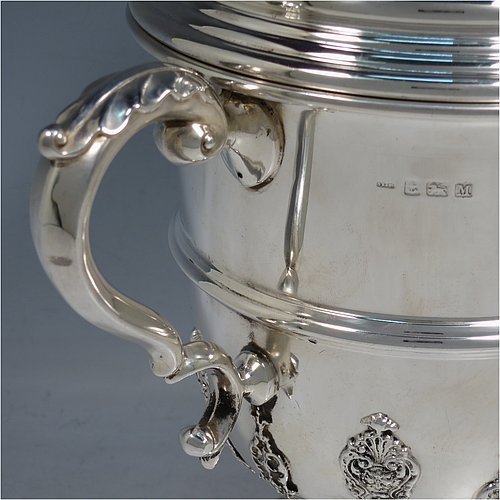 A Sterling Silver trophy cup and cover, in a George II style, having a round body with applied floral strap-work decoration, two scroll side-handles with anthemion leaf thumb-pieces, a central applied girdle band, a pull-off lid with matching applied strap-work and a cast round finial, and all sitting on a stepped pedestal foot. Made by George Bryan & Co., of Birmingham in 1936. The dimensions of this fine hand-made silver trophy cup and cover are height 30 cms (11.75 inches), spread across arms 26.5 cms (10.5 inches), and it weighs approx. 1,132g (36.5 troy ounces).    