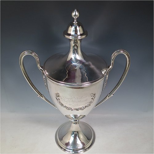 A rare Antique Georgian Sterling Silver large trophy cup and cover, having a neoclassical round plain tapering body with applied laurel-leaf cartouches, with applied reeded borders, two loop side-handles with anthemion leaf shoulders, an original cover with cast finial, and sitting on a round pedestal foot. Made by John Langland II of Newcastle in 1798. The dimensions of this fine hand-made antique silver trophy cup and cover are height 51 cms (20 inches), spread across arms 33 cms (13 inches), and it weighs approx. 3,176g (102 troy ounces). Please note that this trophy is engraved with contemporary presentation inscriptions on both sides. 