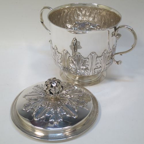 A very handsome Sterling Silver trophy cup and cover, in the shape of a lidded Porringer, having a round body with hand-chased Anthemion leaf decoration, with two scroll side-handles, a lift-off cover with matching decoration and a pierced floral finial, and all sitting on a stepped pedestal foot. Made by Charles Stuart Harris of London in 1925. The dimensions of this fine hand-made antique silver trophy porringer cup are height 18 cms (7 inches), spread across handles 21 cms (8.25 inches), and it weighs approx. 748g (24 troy ounces).   