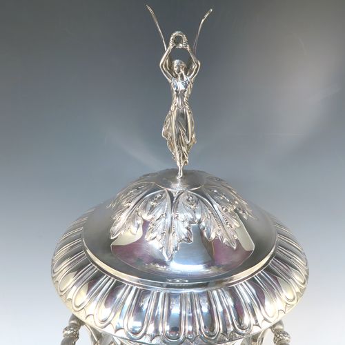 A very handsome and large Antique Edwardian  Sterling Silver trophy cup and cover, having a Campana style round bellied body with hand-chased floral, scroll, and fluted decoration, with two cast side handles, and sitting on a pedestal foot. The pull-off cover with matching decoration and a cast figural finial of the goddess Nike. This beautiful and impressive antique silver trophy cup and cover was made by Jay, Richard Attenborough and Co., of London in 1910. The dimensions of this fine hand-made antique silver trophy cup are height 66 cms (26 inches), spread across handles 29 cms (11.5 inches), and it weighs approx. 3,670g (118 troy ounces).   