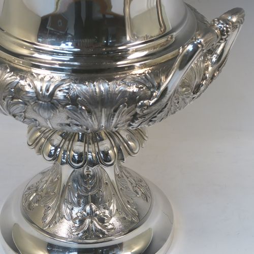 A very handsome and large Antique Edwardian  Sterling Silver trophy cup and cover, having a Campana style round bellied body with hand-chased floral, scroll, and fluted decoration, with two cast side handles, and sitting on a pedestal foot. The pull-off cover with matching decoration and a cast figural finial of the goddess Nike. This beautiful and impressive antique silver trophy cup and cover was made by Jay, Richard Attenborough and Co., of London in 1910. The dimensions of this fine hand-made antique silver trophy cup are height 66 cms (26 inches), spread across handles 29 cms (11.5 inches), and it weighs approx. 3,670g (118 troy ounces).   