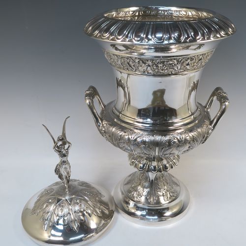 A very handsome and large Antique Edwardian  Sterling Silver trophy cup and cover, having a Campana style round bellied body with hand-chased floral, scroll, and fluted decoration, with two cast side handles, and sitting on a pedestal foot. The pull-off cover with matching decoration and a cast figural finial of the goddess Nike. This beautiful and impressive antique silver trophy cup and cover was made by Jay, Richard Attenborough and Co., of London in 1910. The dimensions of this fine hand-made antique silver trophy cup are height 66 cms (26 inches), spread across handles 29 cms (11.5 inches), and it weighs approx. 3,670g (118 troy ounces).   