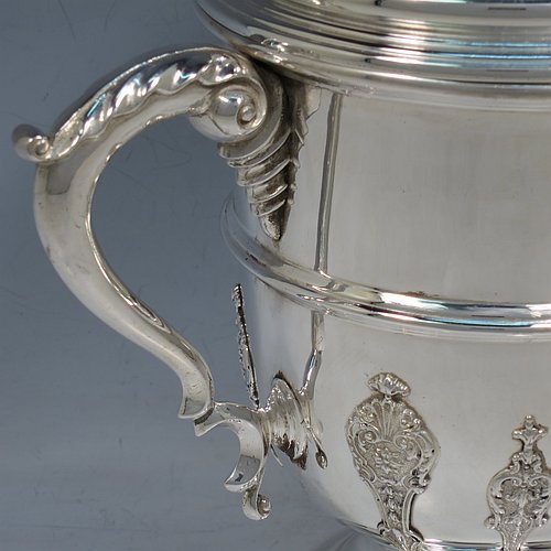 A Sterling Silver trophy cup and cover, in a George II style, having a round body with applied floral strap-work decoration, two scroll side-handles with anthemion leaf thumb-pieces, a central applied girdle band, a pull-off lid with matching applied strap-work and a cast round finial, and all sitting on a stepped pedestal foot. Made by J. A. Restall of Birmingham in 1926. The dimensions of this fine hand-made silver trophy cup and cover are height 26 cms (10.25 inches), spread across arms 24 cms (9.5 inches), and it weighs approx. 830g (27 troy ounces).    