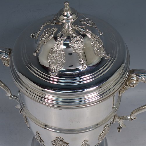 A Sterling Silver trophy cup and cover, in a George II style, having a round body with applied floral strap-work decoration, two scroll side-handles with anthemion leaf thumb-pieces, a central applied girdle band, a pull-off lid with matching applied strap-work and a cast round finial, and all sitting on a stepped pedestal foot. Made by J. A. Restall of Birmingham in 1926. The dimensions of this fine hand-made silver trophy cup and cover are height 26 cms (10.25 inches), spread across arms 24 cms (9.5 inches), and it weighs approx. 830g (27 troy ounces).    