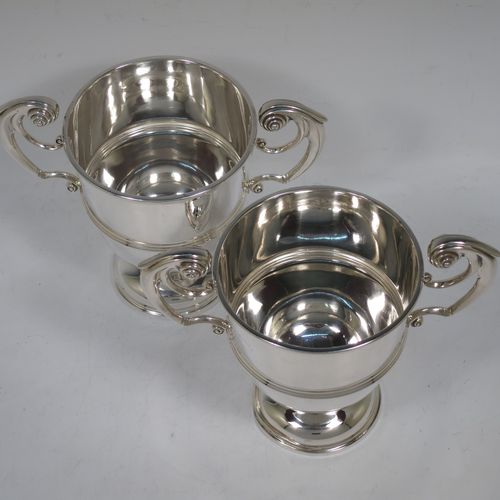 A very handsome Antique Edwardian Sterling Silver pair of trophy cups in a George II style, having plain round bodies with applied reeded borders, two flying scroll side-handles, central applied girdle bands, and all sitting on stepped pedestal feet. Made by Skinner and Co., of Sheffield in 1908. The dimensions of these fine hand-made antique silver trophy cups are height 14.5 cms (5.75 inches), spread across arms 17 cms (7.75 inches), and they weigh a total of approx. 624g (20 troy ounces).   