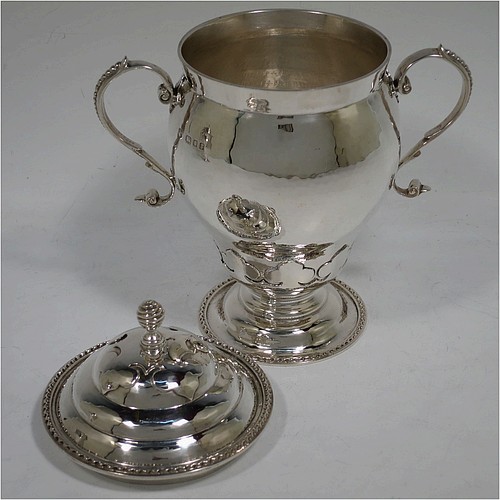 A very unusual pair of Sterling Silver trophy cups and covers, in an Arts and Crafts style, having round bellied bodies with hand-hammered decoration, applied zigzag borders and cut-card work, two side scroll handles with beaded thumb-pieces, removable covers with spiral finials, and all sitting on stepped pedestal feet. Made by D. and J. Wellby of London in 1931. The dimensions of these fine hand-made silver trophy cups and covers are height 17.5 cms (7 inches), spread across arms 15 cms (6 inches), and they weigh a total of  approx. 825g (26.6 troy ounces).   