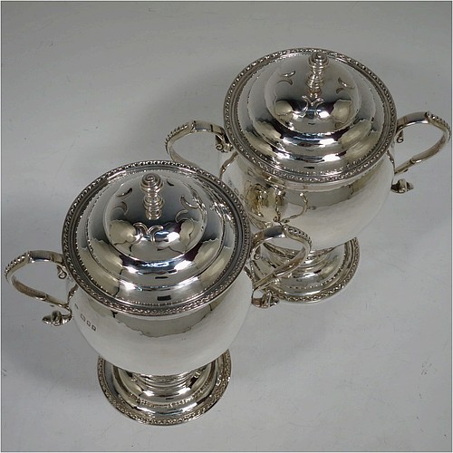 A very unusual pair of Sterling Silver trophy cups and covers, in an Arts and Crafts style, having round bellied bodies with hand-hammered decoration, applied zigzag borders and cut-card work, two side scroll handles with beaded thumb-pieces, removable covers with spiral finials, and all sitting on stepped pedestal feet. Made by D. and J. Wellby of London in 1931. The dimensions of these fine hand-made silver trophy cups and covers are height 17.5 cms (7 inches), spread across arms 15 cms (6 inches), and they weigh a total of  approx. 825g (26.6 troy ounces).   