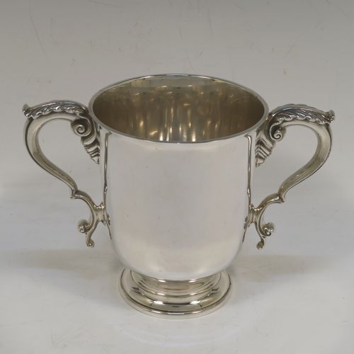 A very handsome and heavy Sterling Silver trophy cup in a George III neoclassical style, having a plain round body with tapering sides, two cast scroll side-handles with anthemion leaf decoration, and all sitting on a stepped pedestal foot. This beautiful sterling silver trophy cup was made by D. and J. Welby of London in 1938. The dimensions of this fine hand-made silver trophy cup are height 12.5 cms (5 inches), spread across arms 18 cms (7 inches), and it weighs approx. 414g (13.4 troy ounces).  