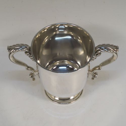 A very handsome and heavy Sterling Silver trophy cup in a George III neoclassical style, having a plain round body with tapering sides, two cast scroll side-handles with anthemion leaf decoration, and all sitting on a stepped pedestal foot. This beautiful sterling silver trophy cup was made by D. and J. Welby of London in 1938. The dimensions of this fine hand-made silver trophy cup are height 12.5 cms (5 inches), spread across arms 18 cms (7 inches), and it weighs approx. 414g (13.4 troy ounces).  