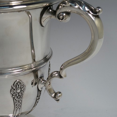 A very handsome Antique Edwardian Sterling Silver trophy cup and cover, in a George II style, having a round body with applied floral strap-work decoration, two scroll side-handles with anthemion leaf thumb-pieces, a central applied girdle band, a pull-off lid with matching applied strap-work and a cast round floral finial, and all sitting on a stepped pedestal foot. Made by Walker and Hall of Sheffield in 1909. The dimensions of this fine hand-made antique silver trophy cup and cover are height 37 cms (14.5 inches), spread across arms 33 cms (13 inches), and it weighs approx. 1,570g (51 troy ounces).    