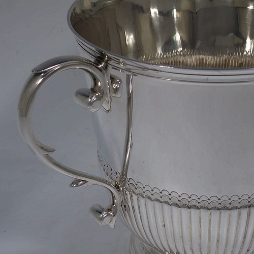 A very handsome Sterling Silver trophy cup in a George III neoclassical style, having a round body with tapering sides and half-fluted decoration, with hand-chased reeded borders, two cast scroll side-handles, and all sitting on a pedestal foot. Made by Charles and Richard Comyns of London in 1921. The dimensions of this fine hand-made silver trophy cup are height 14.5 cms (5.75 inches), spread across arms 24 cms (9.5 inches), and it weighs approx. 683g (22 troy ounces).    