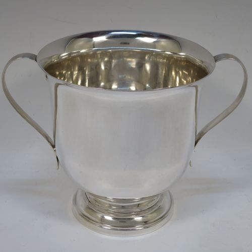 A handsome Sterling Silver trophy cup, having a plain round bellied body, two side-handles with reeded decoration, and sitting on a round stepped pedestal foot. Made by Henry Wilkinson of Sheffield in 1921. The dimensions of this fine hand-made silver trophy cup and are height 15 cms (6 inches), spread across arms 21 cms (8.25 inches), and it weighs approx. 504g (16 troy ounces).   