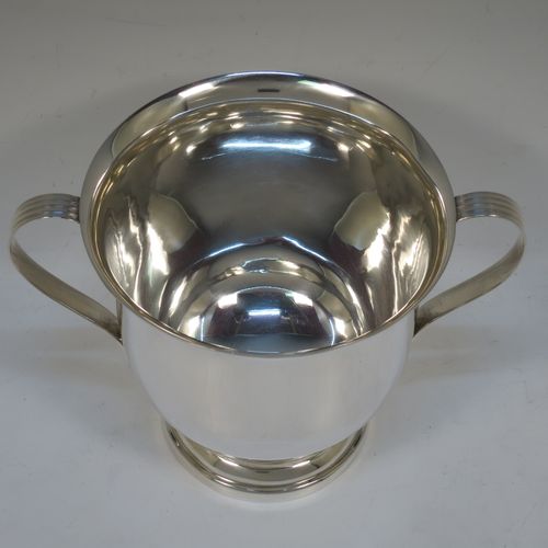 A handsome Sterling Silver trophy cup, having a plain round bellied body, two side-handles with reeded decoration, and sitting on a round stepped pedestal foot. Made by Henry Wilkinson of Sheffield in 1921. The dimensions of this fine hand-made silver trophy cup and are height 15 cms (6 inches), spread across arms 21 cms (8.25 inches), and it weighs approx. 504g (16 troy ounces).   