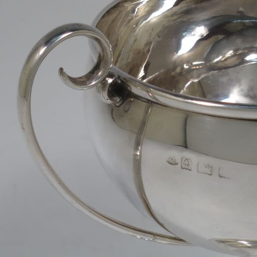 A small but handsome Sterling Silver trophy cup, having a plain round bellied body, with two scroll side-handles, and all sitting on a pedestal foot. Made by the Adie Brothers of Birmingham in 1928. The dimensions of this fine hand-made silver trophy cup are height 15 cms (6 inches), spread across arms 15 cms (6 inches), and it weighs approx. 148g (4.8 troy ounces).   